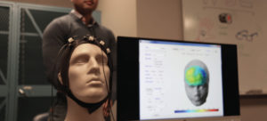 A mannequin head with electrodes attached next to a computerized map of the head.